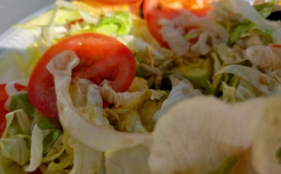 Nahaufnahme eines gemischten Salats mit geschnittenen Tomaten, Eisbergsalat und möglicherweise anderem Gemüse. Die Farben sind lebendig und heben die Frische der Zutaten hervor. Das Bild scheint bei natürlichem Licht aufgenommen worden zu sein, wodurch die Textur des Salats und der Tomaten hervorgehoben wird.