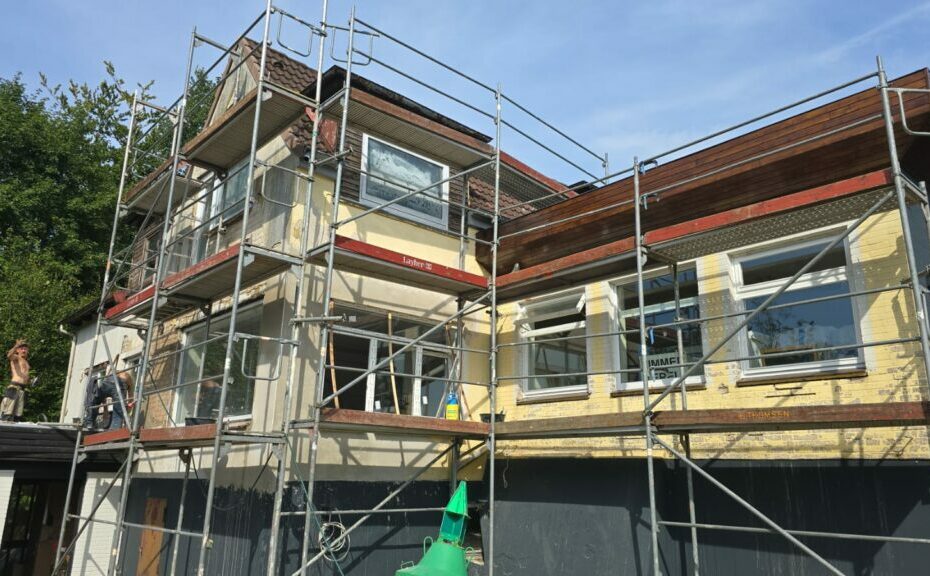 Haus mit Gerüst während der Renovierung, Handwerker arbeiten an der Fassade, Bauarbeiten sichtbar, modernes Wohnhaus.